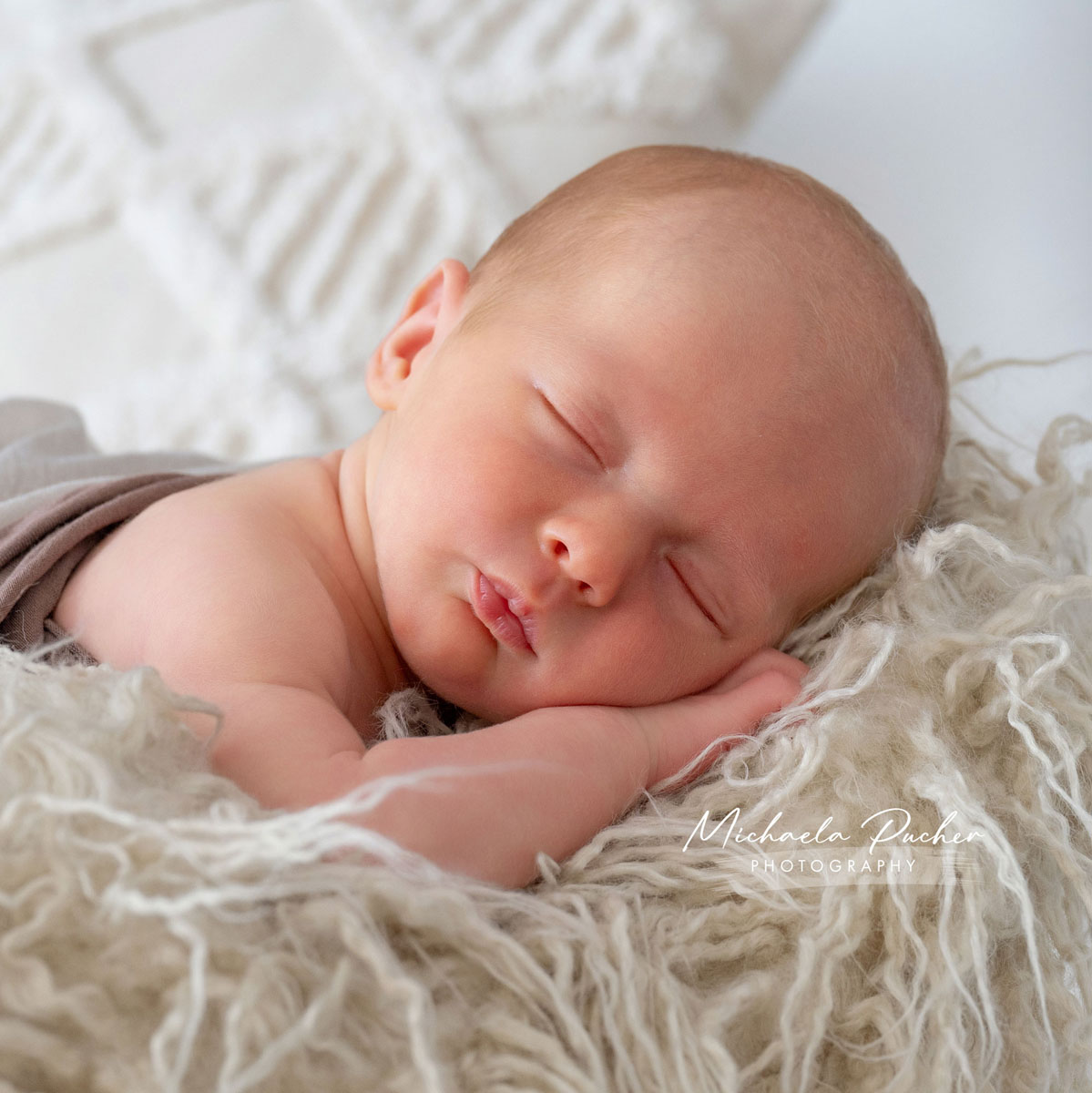 Schlafendes Neugeborenes liegt auf einer weichen flauschigen Unterlage, den Kopf auf die Hand gebettet, in warmem Naturlicht.